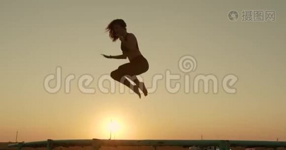 女孩在海滩上日落的阳光下跳上蹦床。视频