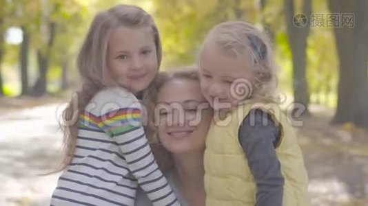 在秋天公园里，两个快乐的白种人小妹妹拥抱着卷曲的金发女人的特写肖像。 可爱的微笑视频
