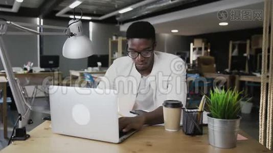 非洲商人正在用笔记本电脑工作，并在现代办公室接听电话视频