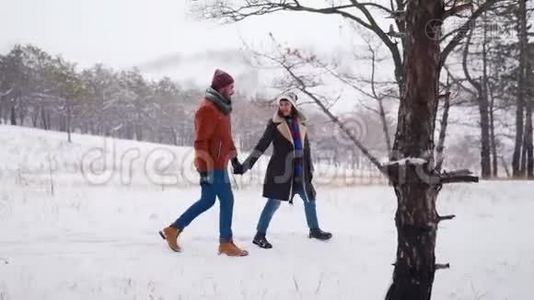 年轻可爱的一对夫妇在下雪的公园里散步。 男人牵着他的女朋友的手，享受冬天的雪视频