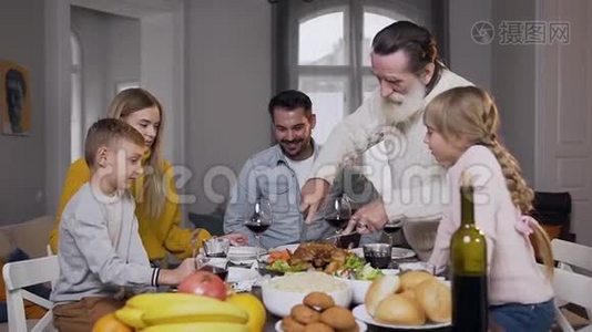 呼吁60岁的胡子爷爷雕刻美味的烤火鸡，为他的家人聚集在餐桌旁视频