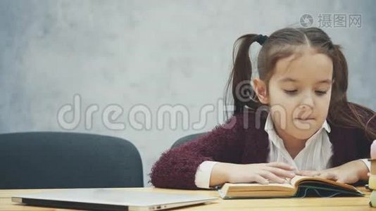 一个女学生坐在桌子旁。 在这段时间里，他读了一本书。 合上书拿着笔记本电脑。 很开心。 在一个视频
