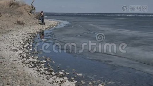 一对年轻夫妇沿着冰封的河流的岸边散步，阳光明媚的春天视频