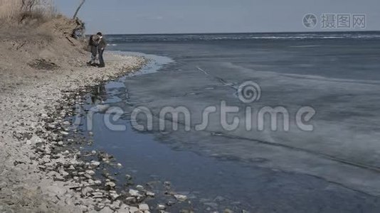 一对年轻夫妇沿着冰封的河流的岸边散步，阳光明媚的春天视频