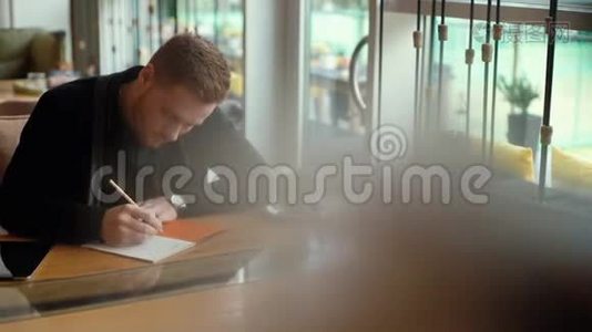 年轻的帅哥正在写蓝图，坐在舒适的咖啡馆里的桌子旁视频