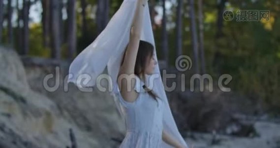 微笑的白种人女孩站在森林里，举起手里拿着浅白色的围巾。 美丽的女人视频