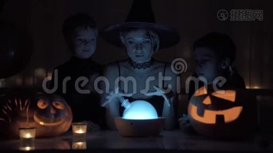 妈妈和两个儿子在万圣节扮演女巫。 晚上桌子上有一盏神奇的灯和一个南瓜。视频