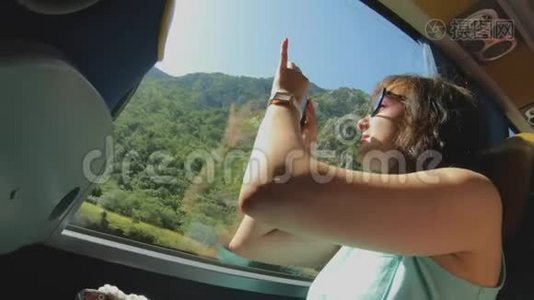 带智能手机的旅游女孩通过公共汽车窗口拍摄自然景观。 观光旅行和旅游视频
