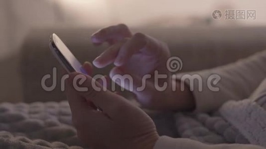 现代概念：特写女人`双手坐在沙发上，用她的智能手机，手指放在屏幕上。视频