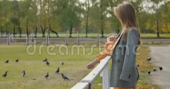 在秋天公园里，一位有着棕色长发的有魅力的高加索女人站在畜栏旁边。 很漂亮视频