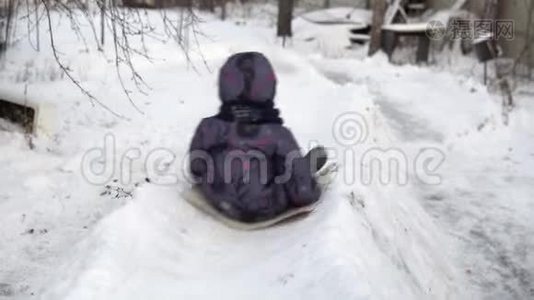 一个孩子在雪地滑梯上翻滚。 冬天在街上玩。 在寒冷的冬天，孩子穿着一件夹克和一件视频