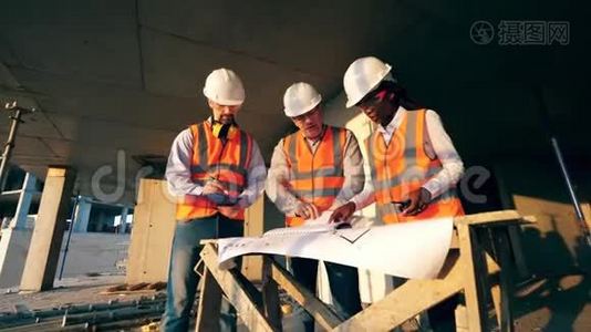三个工人看一个施工现场的蓝图。 现代施工现场的施工工人..视频