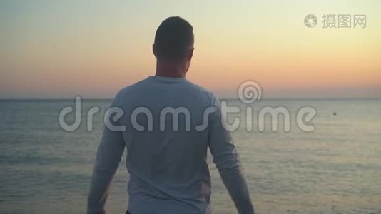 一个年轻人站在海上日落的背景上，举起双手，显示出自由的迹象。视频