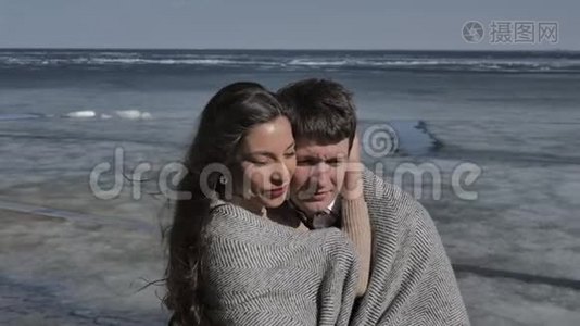 年轻夫妇拥抱着，背景是一条覆盖着冰的河流，阳光明媚的春天视频