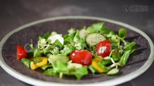 女人在蔬菜沙拉中加入盐与蔬菜，黄瓜，西红柿，胡椒。 把落在石盘上的绿色沙拉混合在一起视频