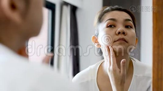 中年亚洲女人看着镜子里的皱纹和面部问题视频