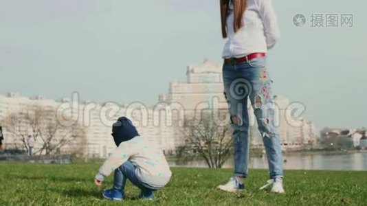 小男孩背对着镜头坐在草地上玩栗子和他年轻的妈妈视频