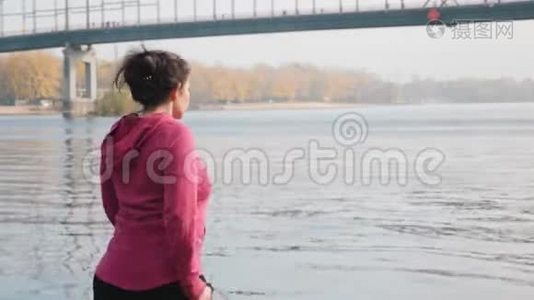 在后侧，沿着年轻胖乎乎的女孩的视线，独自在河和城市公园里做晨间北欧散步运动视频