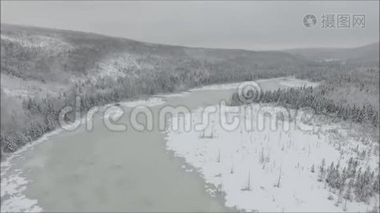 冬季寒冷的山山景观中，一架空中无人机在白雪覆盖的湖河和松树上盘旋视频