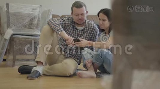 一个快乐的高加索家庭的特写镜头，坐在客厅的地板上，带着新的家具，使用智能手机视频