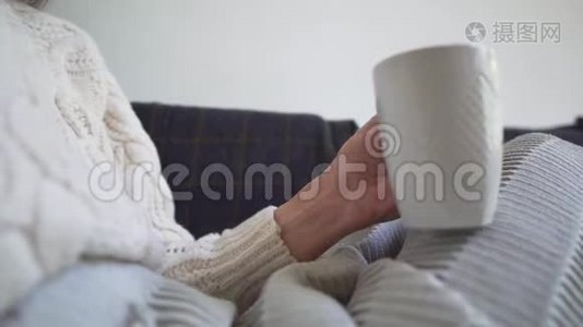 特写镜头——女孩端着一杯新鲜咖啡，藏在毯子里，在寒冷的秋日，坐在舒适的沙发上视频