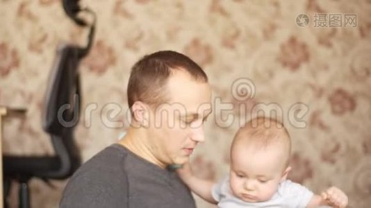 父亲坐在地板上，手里拿着他的孩子，和他的儿子玩耍，亲吻他，他们都很高兴视频
