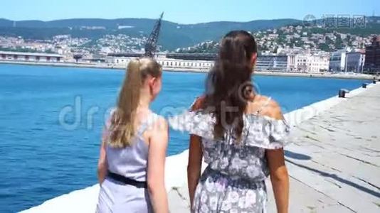 女孩们沿着靠近海边的泊位漫步，与山丘上的城市景观相对视频