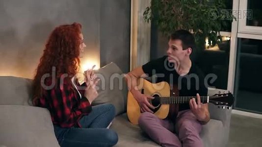 一位丈夫正在为他的妻子唱一首歌，弹一把吉他，妻子也和他一起坐在沙发上唱歌视频