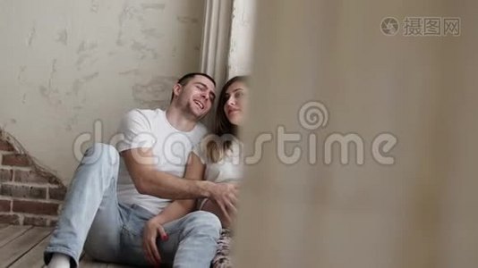 幸福的夫妻正坐在地板上，丈夫抚摸着怀孕的妻子的肚子视频