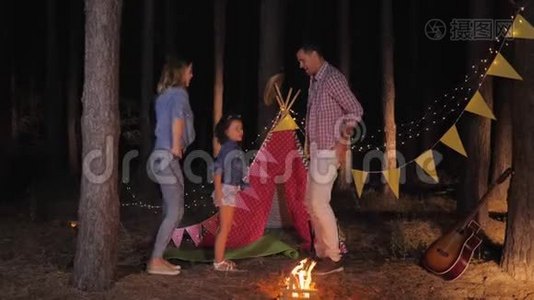 家庭度假时，快乐的父母和快乐的女儿一起在森林野餐时一起跳舞，露营视频