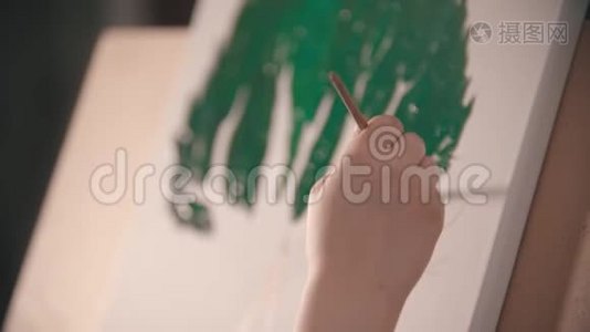 一个年轻的女人`她的手在画布上画了一顶绿色的树冠视频