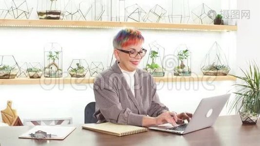 自信的戴眼镜的高级妇女坐在白色办公室的笔记本电脑上视频