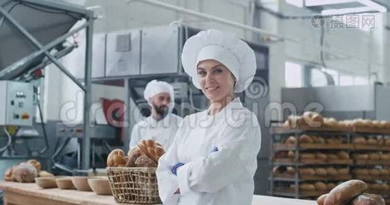 一位令人惊叹的女士面包师的商业面孔直视着相机，微笑着可爱的背景，他的同事面包师。视频