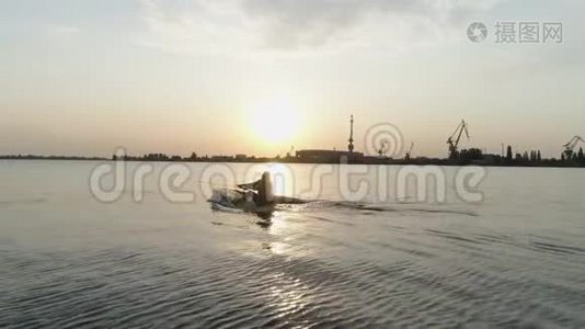 鸟瞰图，冲浪者在摩托艇后面沿着河边骑着尾板，在日落时手握绳柄视频