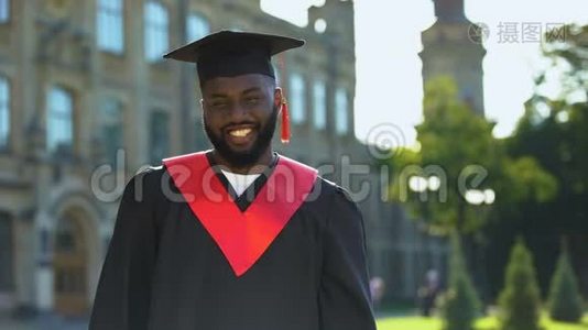 毕业礼服上的黑人男性在大学背景上微笑着视频