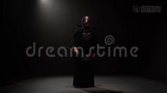剑道拳手在聚光灯下的黑暗工作室用卡塔纳剑表演武术。视频
