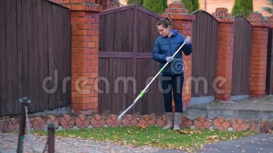 女孩用耙子从房子前面的草坪上摘下落叶视频