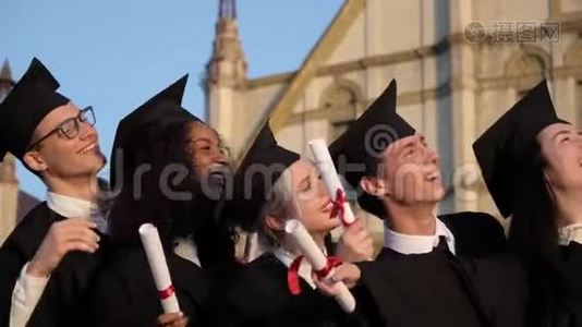 混合种族毕业的朋友穿着黑色传统长袍和帽子制作自拍智能手机。视频