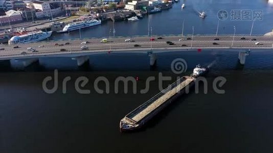 货物驳船在桥下航行。 桥上的城市交通。视频