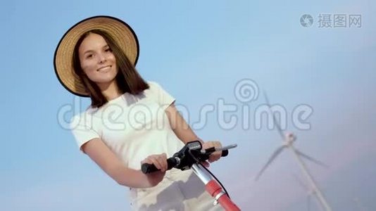 一个女孩戴着一顶优雅的草帽，在风电场的背景辆电动滑板车的肖像。视频