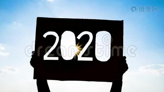手拿回收纸板的剪影，用2020年的文字在蓝天背景和阳光照耀的文字。 康塞普视频