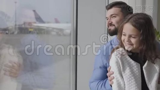 一个快乐的白人男人和他的女儿坐在机场窗台上看着跑道。 小可爱视频