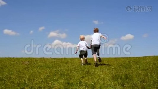 两个小男孩在绿色的草地上奔跑，手牵着蓝天和云彩的背景视频