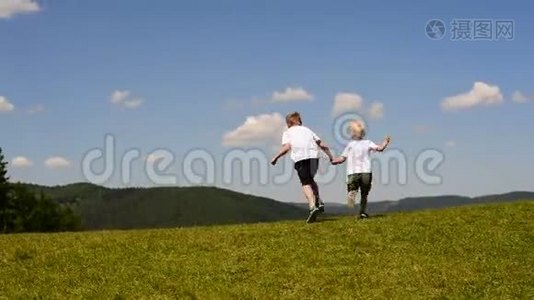 两个小男孩在绿色的草地上奔跑，手牵着蓝天和云彩的背景视频