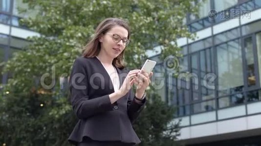 微笑的女商人在办公楼附近浏览智能手机视频