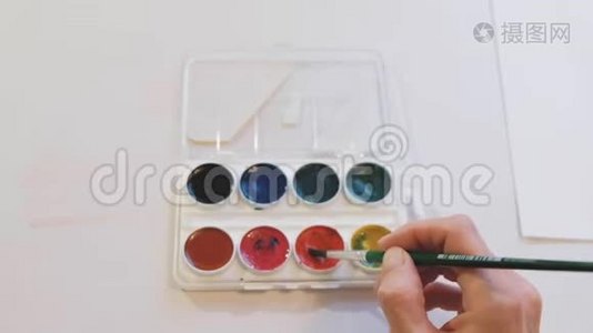 一个水彩调色板的颜色和一个女人`手把刷子投入红色。视频