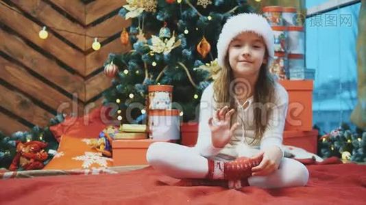 4K视频年轻女性戴着圣诞帽挥舞着手，邀请每个人与她在木制背景下庆祝。视频