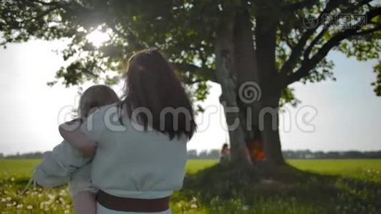 妈妈穿着白色连衣裙，女儿抱着她去了一棵老橡树。视频