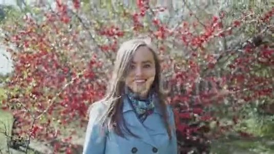 穿着蓝色雨衣的快乐女孩穿过春天的公园，走过一棵开着红花的树视频