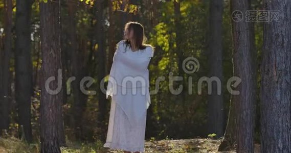穿着白色披肩的白种人迷人的女人站在夏日森林的阳光下四处张望视频